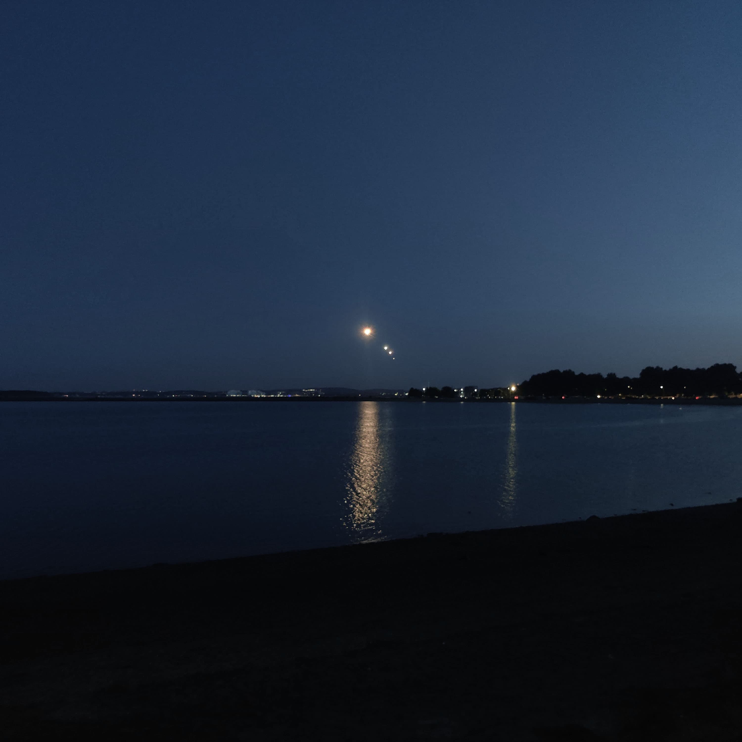 planes, visible as points of light in the night sky, lining up to approach the runway